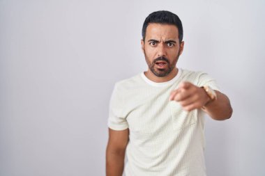 Hispanic man with beard standing over isolated background pointing displeased and frustrated to the camera, angry and furious with you 