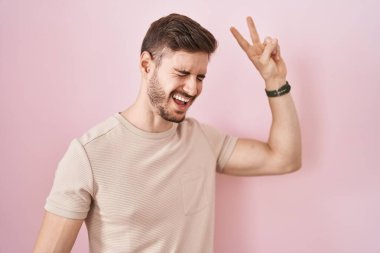 İspanyol sakallı bir adam pembe arka planda dans ediyor mutlu ve neşeli, hareketli ve kendinden emin, müzik dinliyor. 