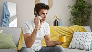 Genç İspanyol adam akıllı telefondan konuşuyor evde kahve içerken hava üflüyor.