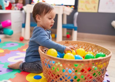 Anaokulunda yerde oturmuş toplarla oynayan sevimli İspanyol çocuk.