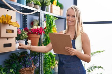 Genç sarışın, gülümseyen çiçekçi. Kendine güvenen. Çiçekçi dükkanında rafları düzenleyen.