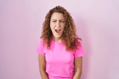 Young caucasian woman standing over pink background angry and mad screaming frustrated and furious, shouting with anger. rage and aggressive concept. 