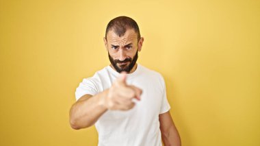 Ciddi bir ifadeyle ayakta duran İspanyol genç adam izole edilmiş sarı arka planda kamerayı işaret ediyor.