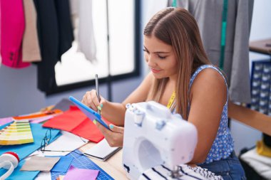 Young beautiful hispanic woman tailor smiling confident drawing on touchpad at tailor shop