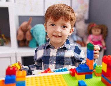 Anaokulundaki masada oturan, inşaat bloklarıyla oynayan sevimli çocuk.