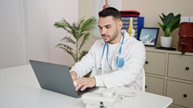 Young hispanic man doctor using laptop working at clinic