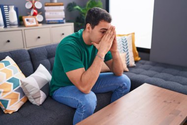 Young hispanic man stressed sitting on sofa at home