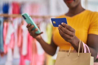 African american woman customer holding shopping bags using smartphone and credit card at clothing store