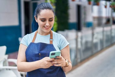 Young caucasian woman waitress smiling confident using smartphone at coffee shop terrace