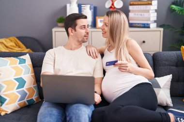 Kadın ve erkek, evde bebek beklerken dizüstü bilgisayar ve kredi kartı kullanıyor.