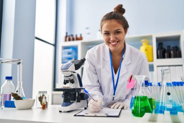 Genç, güzel İspanyol bilim kadını gülümseyen kendine güvenen yazma raporu laboratuvarda çalışıyor.