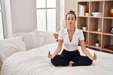 Young caucasian woman doing yoga exercise sitting on bed at bedroom
