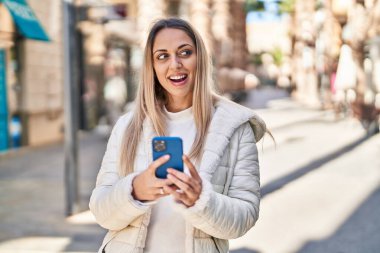 Sokakta akıllı telefon kullanan kendine güvenen genç bir kadın.