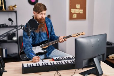 Genç kızıl saçlı müzisyen müzik stüdyosunda elektro gitar çalıyor.