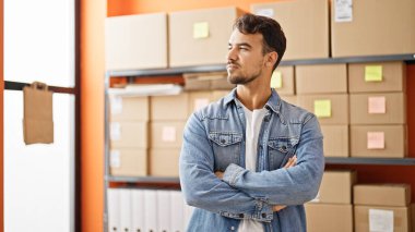 Young hispanic man ecommerce business worker standing with arms crossed gesture at office