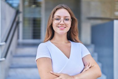 Sokakta kollarını kavuşturmuş genç sarışın kadın.