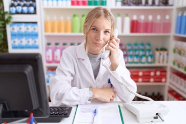 Eczanede çalışan genç, beyaz bir kadın telefonla konuşuyor. Uykulu ve yorgun görünüyor. Yorgunluktan ve akşamdan kalmalıktan yorgun.. 