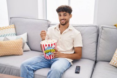 Young arab man eating popcorn watching movie at home