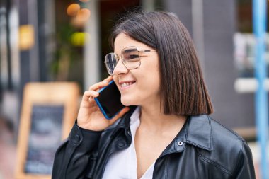 Genç, güzel, İspanyol bir kadın gülümsüyor ve caddede akıllı telefondan konuşuyor.