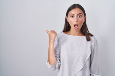 Beyaz arka planda duran Latin kökenli genç kadın elleri yana doğru işaret ederek şaşırdı, ağzı açık hayret içinde kaldı.. 
