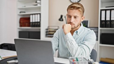 Ofiste çalışan genç beyaz bir iş adamı dizüstü bilgisayar kullanıyor.