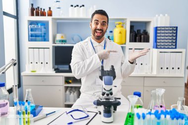 Laboratuvarda çalışan sakallı genç İspanyol adam kameraya hayret ediyor ve gülümsüyor.. 