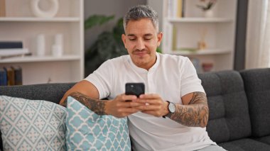 Evdeki kanepede oturan, akıllı telefon kullanan genç bir İspanyol.