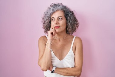 Middle age woman with grey hair standing over pink background thinking worried about a question, concerned and nervous with hand on chin 