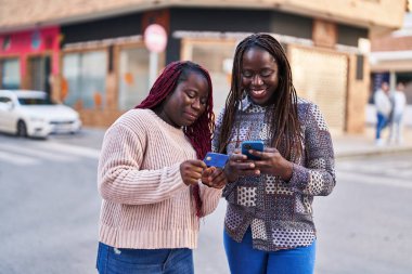 Sokakta akıllı telefon ve kredi kartı kullanan Afrikalı Amerikalı kadın arkadaşlar