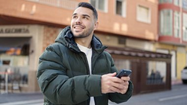 Kahve dükkanının terasında kendine güvenen genç İspanyol adam akıllı telefon kullanıyor.