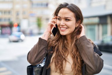Genç, güzel, İspanyol bir kadın gülümsüyor ve caddede akıllı telefondan konuşuyor.
