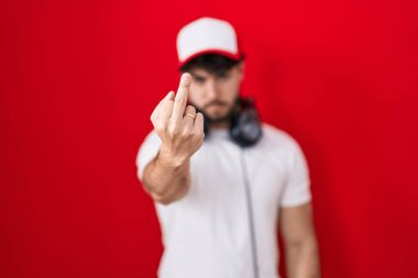 Hispanic man with beard wearing gamer hat and headphones showing middle finger, impolite and rude fuck off expression 