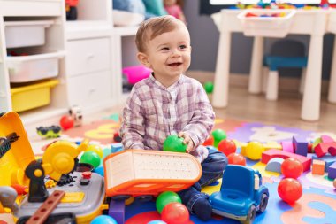 Anaokulunda yerde taşaklarıyla oynayan sevimli beyaz çocuk.