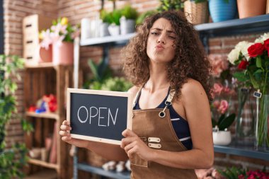 Çiçekçide çalışan kıvırcık saçlı İspanyol kadın elinde açık tabelayla kameraya bakıp öpüşürken çok güzel ve seksi görünüyor. aşk ifadesi. 
