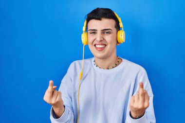 Non binary person listening to music using headphones showing middle finger doing fuck you bad expression, provocation and rude attitude. screaming excited 