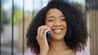 Afro-Amerikalı kadın gülümsüyor. Akıllı telefondan konuşuyor.