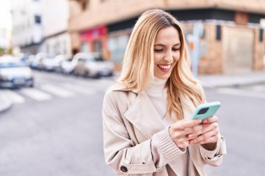 Sokakta akıllı telefon kullanan, kendine güvenen genç sarışın kadın.
