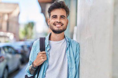 Young hispanic man student smiling confident wearing backpack at street