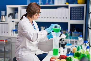 Laboratuvarda test tüpüne sıvı döken orta yaşlı kadın bilim adamı.