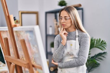 Young woman artist looking draw with doubt expression at art studio