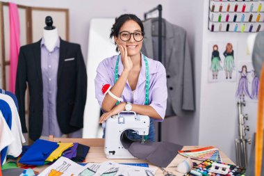 Güzel İspanyol kadın terzi dükkanında dikiş makinesine yaslanarak gülümsüyor.