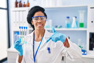 Orta yaşlı İspanyol kadın laboratuvarda çalışıyor. Kendini mutlu ve gururlu bir şekilde gösteren birini işaret ediyor. 