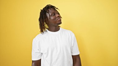 Afro-Amerikalı bir adam gülümsüyor, kendinden emin, izole edilmiş sarı arka plana bakıyor.