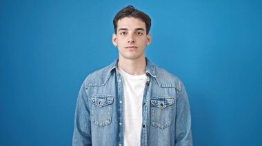 Soyutlanmış mavi arka planda ciddi bir ifadeyle duran İspanyol genç adam.