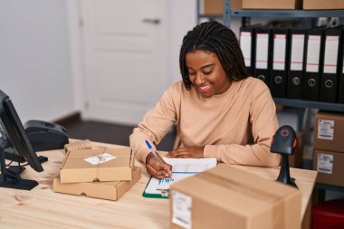 African american woman ecommerce business worker writing on clipboard at office