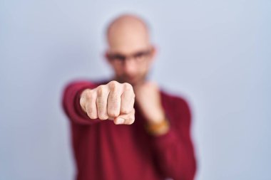 Beyaz arka planda sakallı genç bir adam. Gözlük takıyor. Yumruk yumruğa dövüşüyor. 