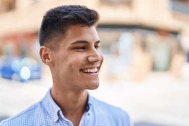 Young hispanic man smiling confident looking to the side at street