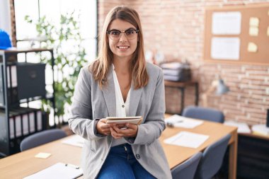 Young hispanic woman working at the office wearing glasses with a happy and cool smile on face. lucky person. 