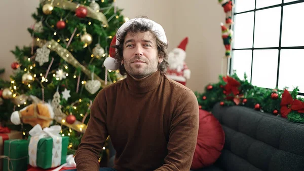 自宅でリラックスした表情でクリスマスツリーでソファーに座っている若いヒスパニック男性 — ストック写真