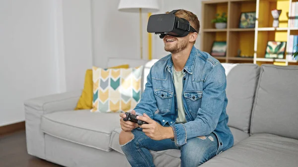 Young caucasian man playing video game using virtual reality glasses and joystick at home